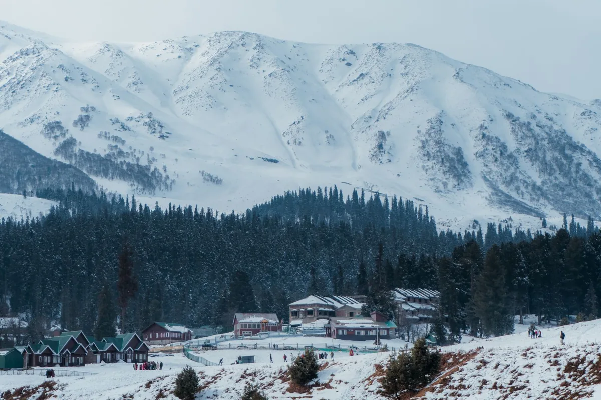 Snow-covered Gulmarg with pine forest and wooden cabins below the mountains, a stop on the Kashmir group trip from Delhi