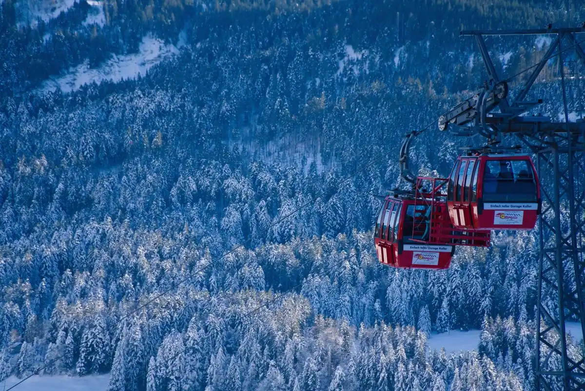 Red gondola cabin over a snowy mountain forest, illustrating a Gulmarg cable-car booking day for families