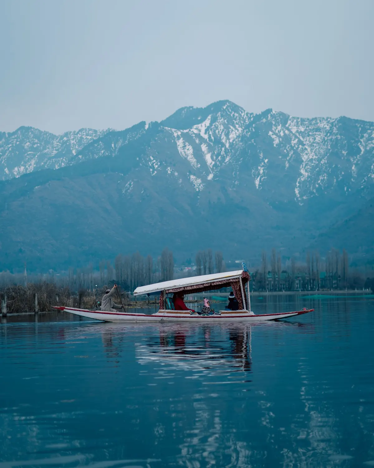 Private canopy shikara with passengers on a calm Kashmir lake and mountain backdrop