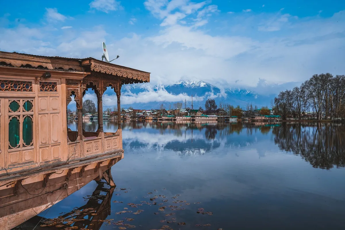 Carved wooden houseboat docked on a Srinagar lake with snow-capped mountains across the water