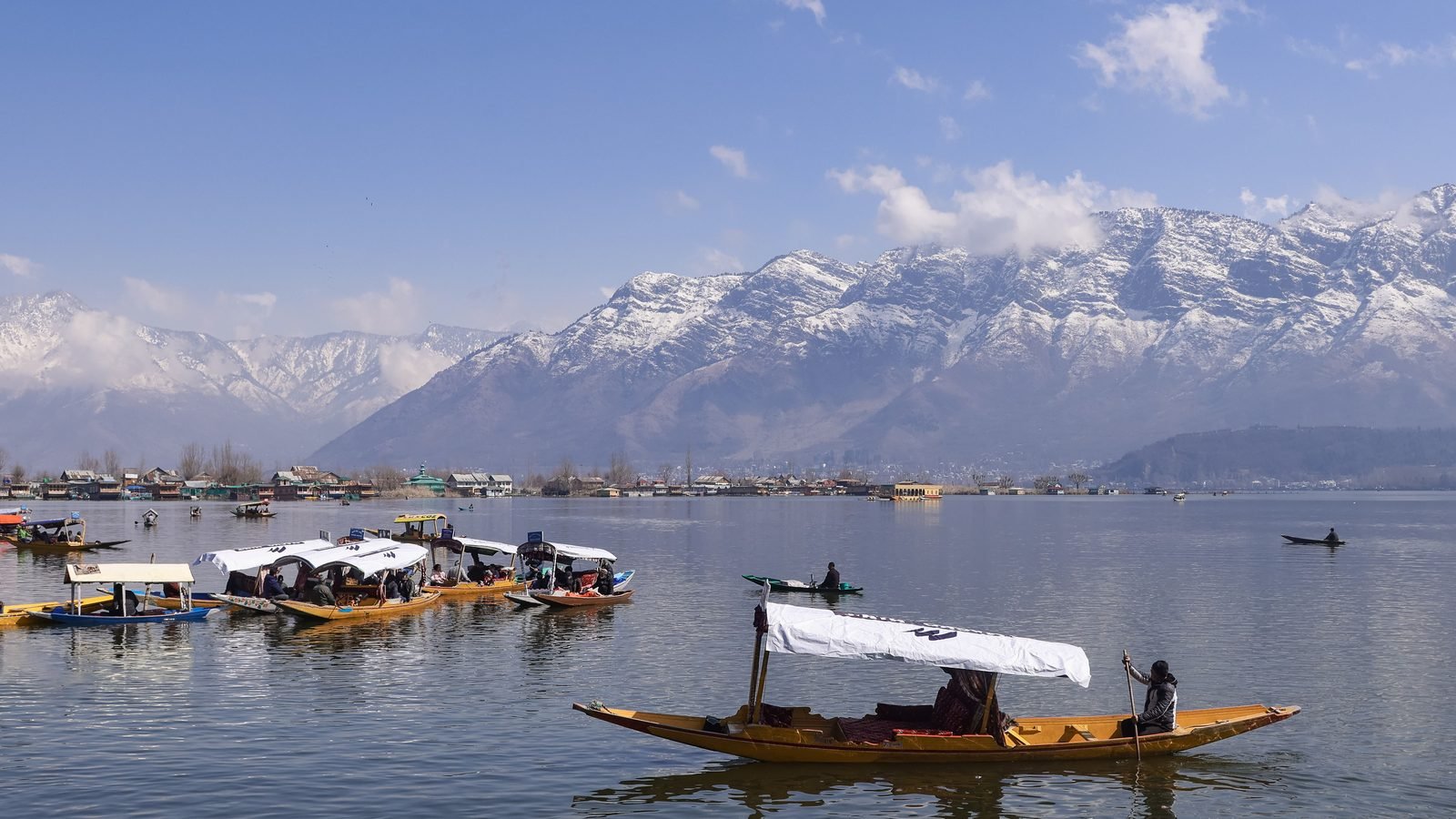 Shikaras with white canopies on a calm Dal Lake in Srinagar with snow-covered mountains behind and houseboats along the far shore