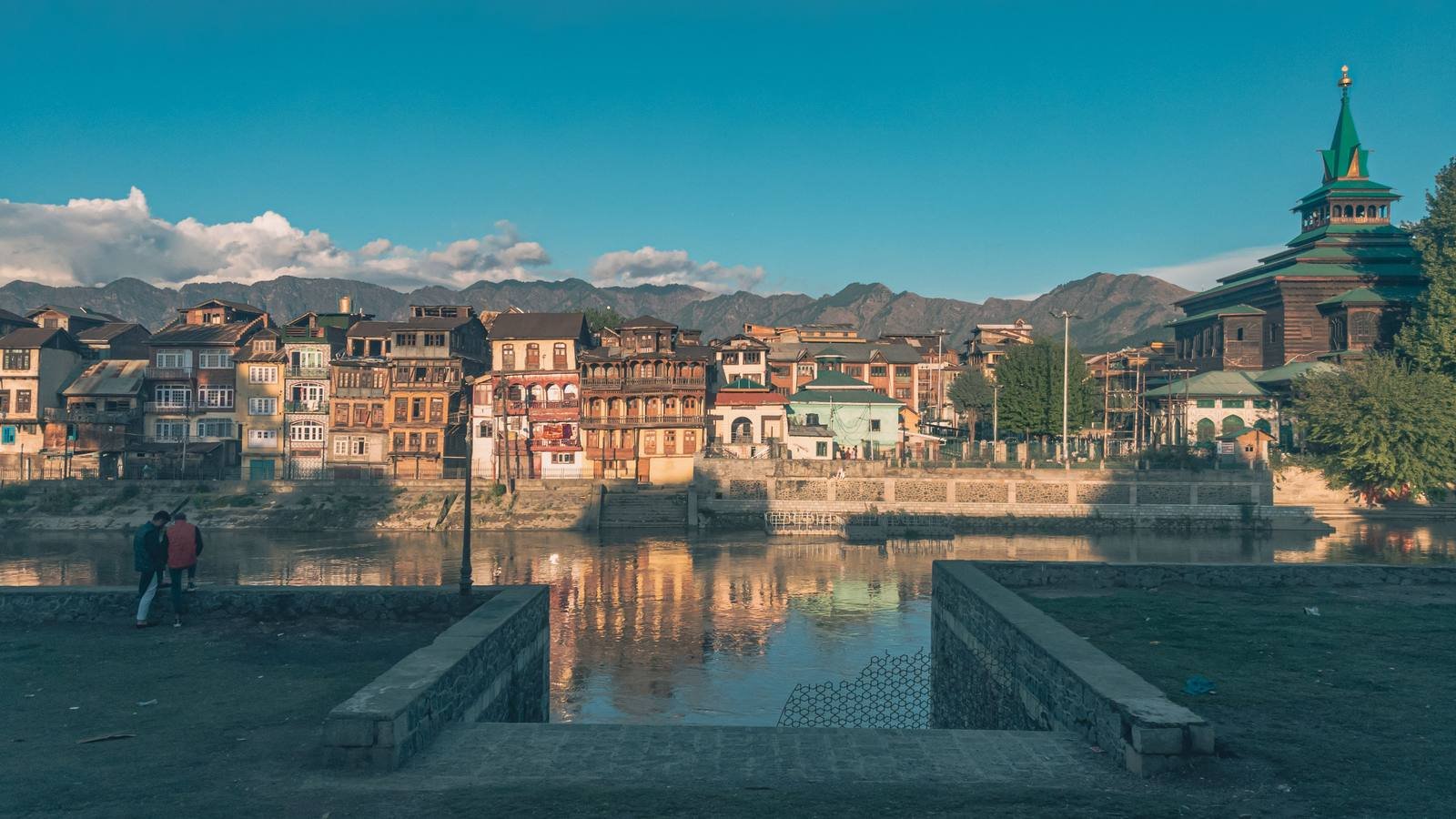 Khanqah-e-Moula with its green spire beside old wooden houses on the Jhelum river in Srinagar, mountains behind