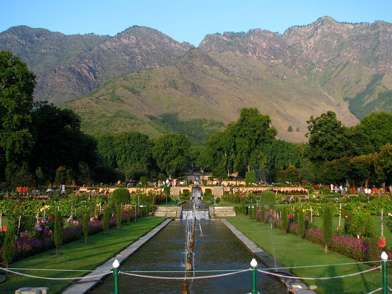 Tourists walking in Nishat Bagh Mughal garden in Srinagar with mountains behind